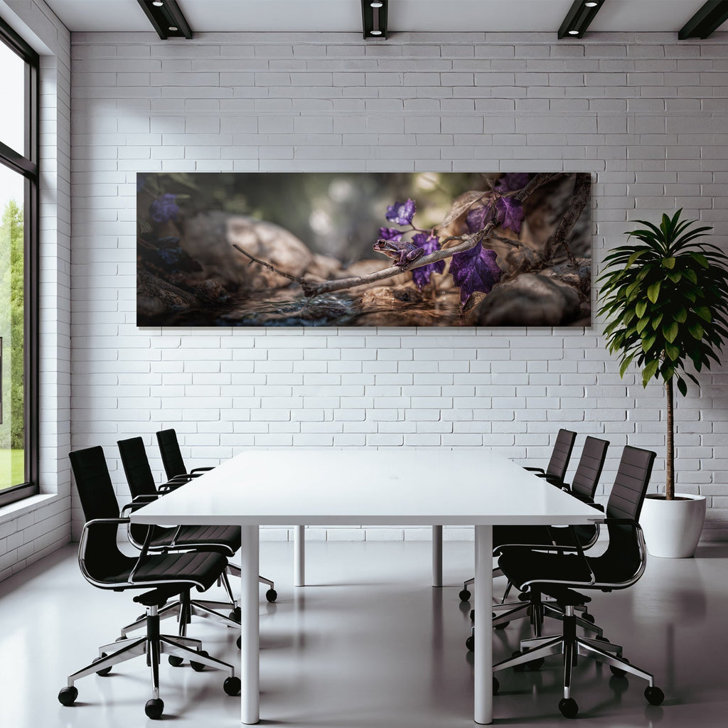 Frog on a branch surrounded by bright purple leaves with a background of water and stones